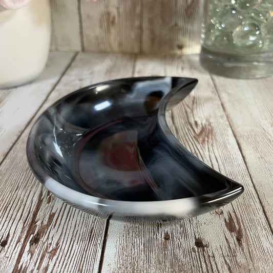 Crescent moon dish on a wooden surface with flowers and a jar in the background