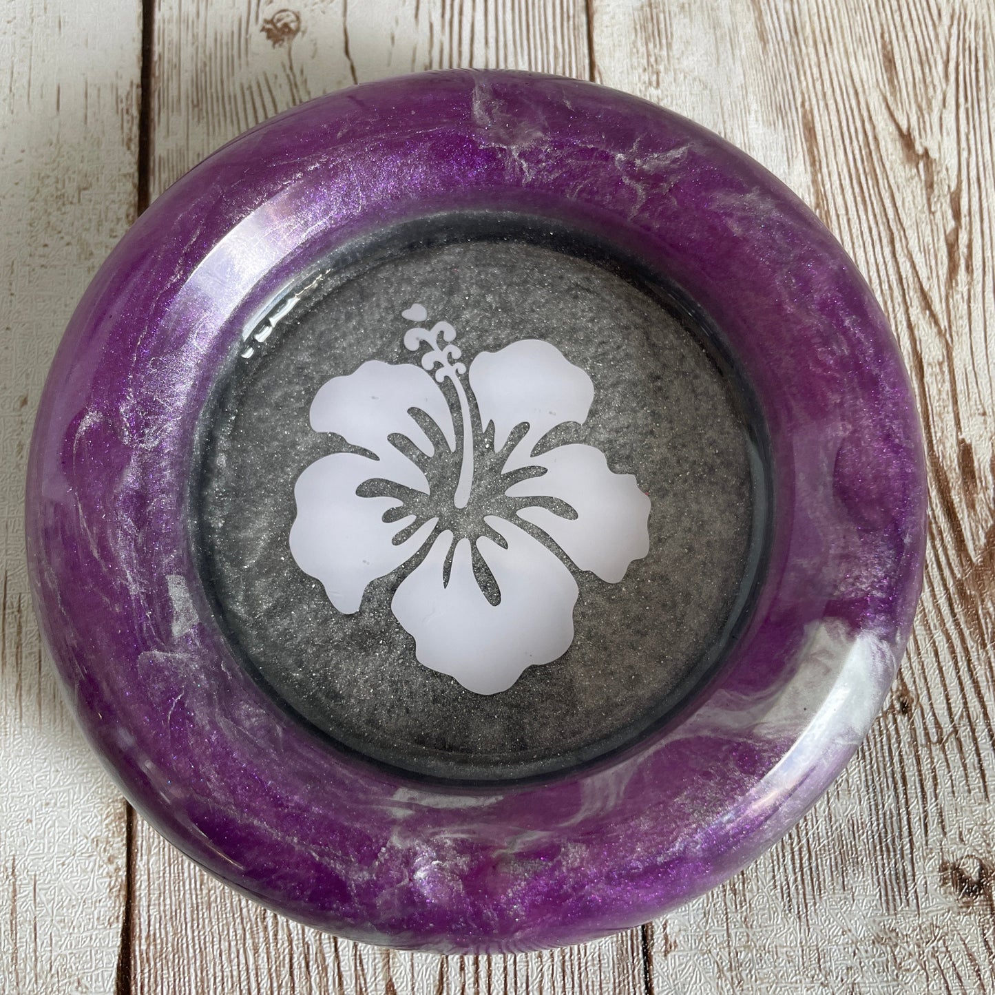 Decorative ashtray with a purple rim and white floral design on a wooden surface
