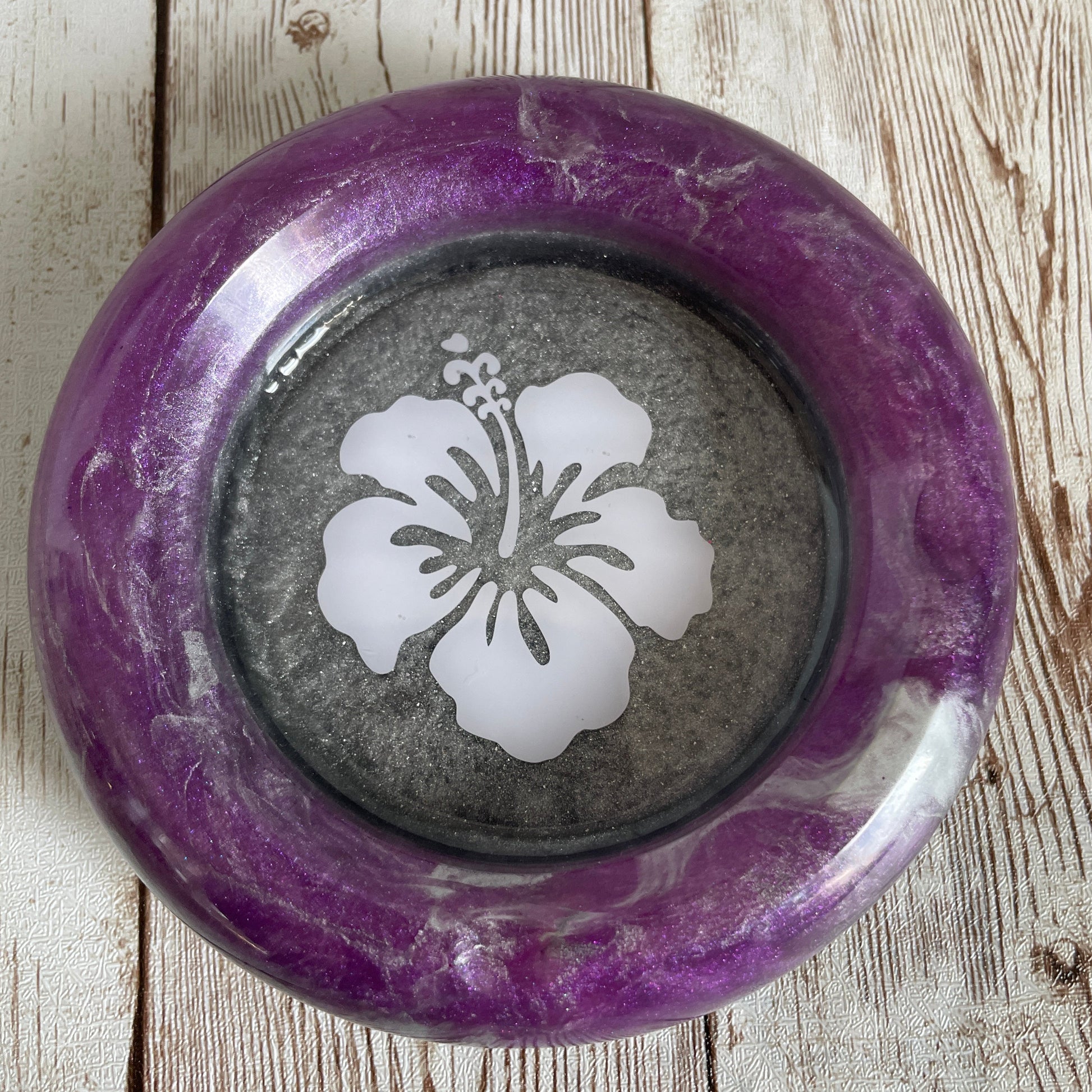 Decorative ashtray with a purple rim and white floral design on a wooden surface
