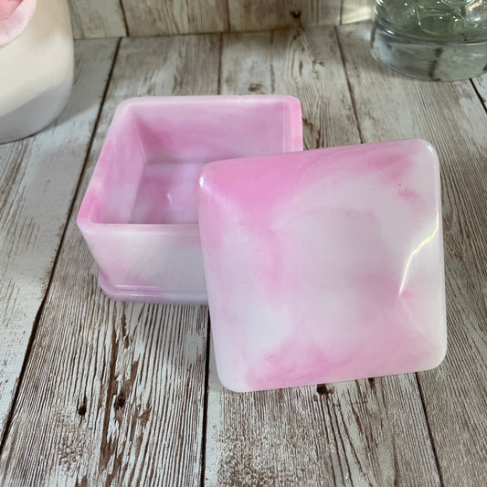 Pink and white marbled resin box on a wooden surface with flowers and a glass container.