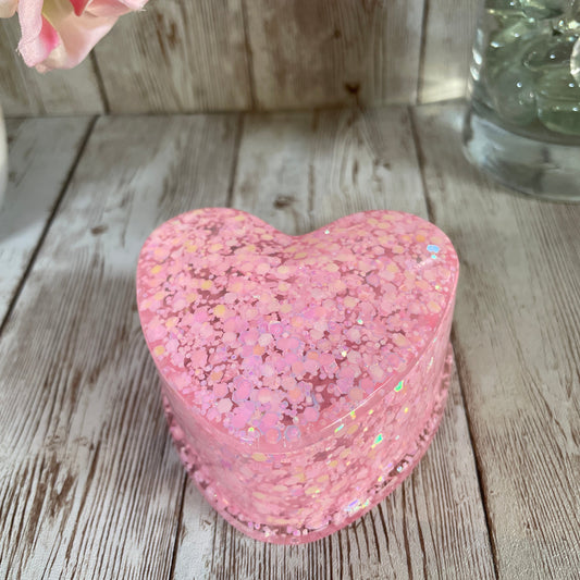 Pink glittery heart-shaped jewelry box on a wooden surface with a blurred background